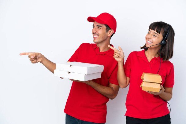 Junges Lieferpaar mit Pizzen und Burgern auf weißem Hintergrund, die Hände zur Seite ausstreckend, lädt zum Kommen ein - Foto, Bild