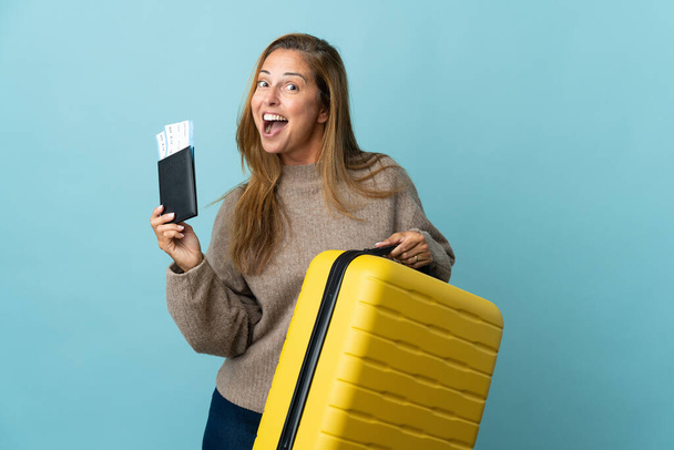 Viaggiatore donna di mezza età con una valigia isolata su sfondo blu in vacanza con valigia e passaporto - Foto, immagini