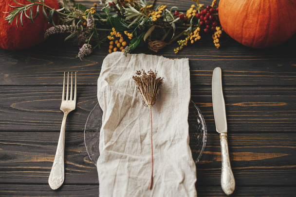 Thanksgiving dinner rustic table setting. Modern plate with vintage cutlery, linen napkin, herb on wooden table with pumpkins and autumn flowers arrangement. Eco friendly farmhouse autumn catering - Photo, Image