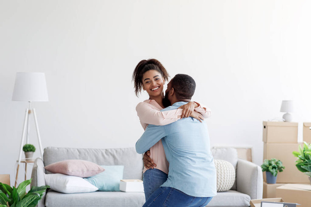 Heureux jeune couple noir excité célébrant l'achat d'une nouvelle maison, mari soulevant femme, dans le jour de déménagement - Photo, image