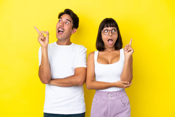 Young mixed race couple isolated on yellow background thinking an idea pointing the finger up - Φωτογραφία, εικόνα