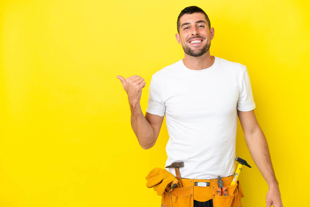 young electrician caucasian man isolated on yellow background pointing to the side to present a product - Φωτογραφία, εικόνα