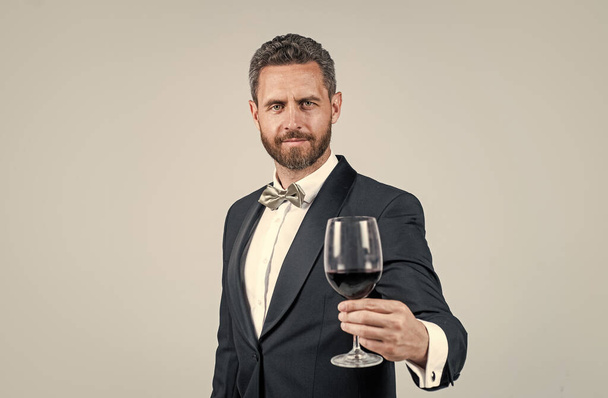 man wear office costume. formal event. businessman drink red wine. cheers for happy valentines day. alcohol drinking. handsome male on romantic date. unshaven man with wine glass. sommelier - Фото, зображення