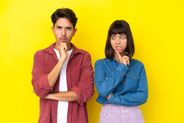 Young mixed race couple isolated on yellow background having doubts while looking up - Foto, Imagen
