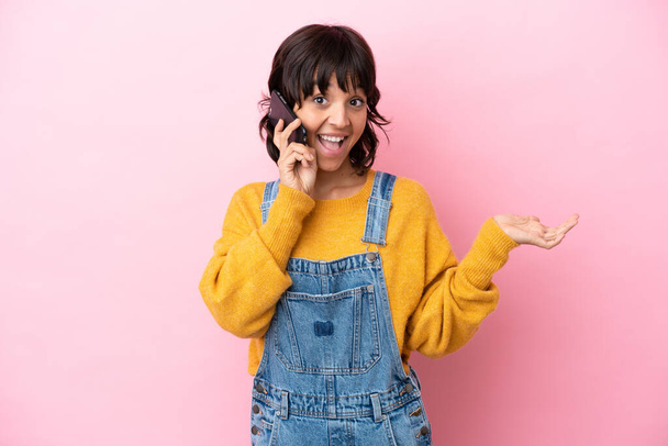 Young woman with overalls isolated background keeping a conversation with the mobile phone with someone - Photo, Image
