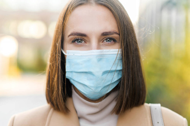 Woman wearing protective medical mask looks at the camera - Foto, afbeelding