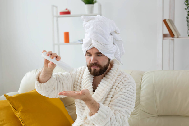 Bearded man holds white bottle cream or gel for skin care. Spa, body and skin care for man concept - Photo, Image