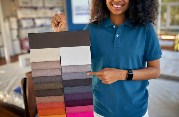 Una asistente de ventas afroamericana muestra muestras de telas de tapicería en una cama, colchón y tienda de almohadas. - Foto, Imagen