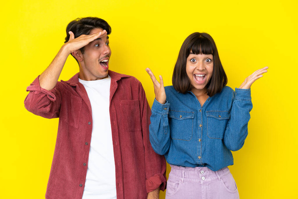 Young mixed race couple isolated on yellow background with surprise and shocked facial expression - Фото, изображение