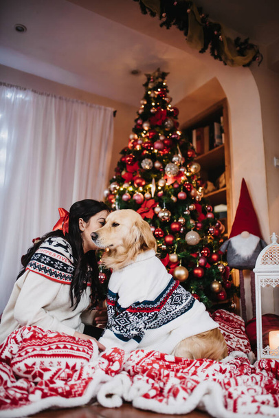 A female playing with her golden retriever dog beside a colorful Christmas Tree at Christmas eve - Fotó, kép