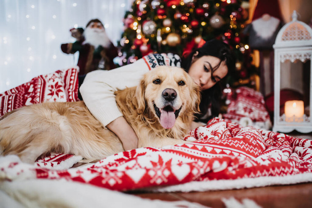 A female playing with her golden retriever dog beside a colorful Christmas Tree at Christmas eve - Foto, Imagen