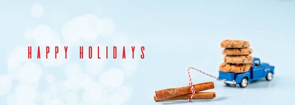 A toy car carries cookies with chocolate and cinnamon sticks on a blue background. Holiday card for New Year and Christmas - Foto, afbeelding
