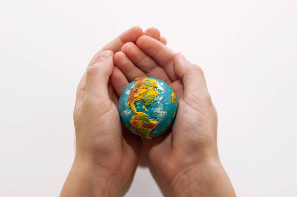 a small plasticine globe in the hands of a child on a white background - Zdjęcie, obraz