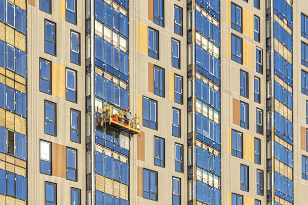 Рабочие, одетые в униформу, в строительную колыбель, на фасаде высотного здания, выполняют свою работу - Фото, изображение