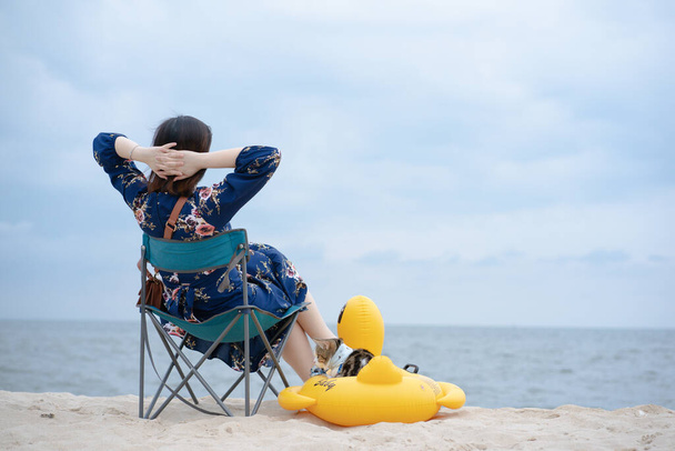 femme se détendre et s'asseoir sur la chaise de plage avec son chat s'asseoir sur l'anneau en caoutchouc de canard sur la plage de sable - Photo, image