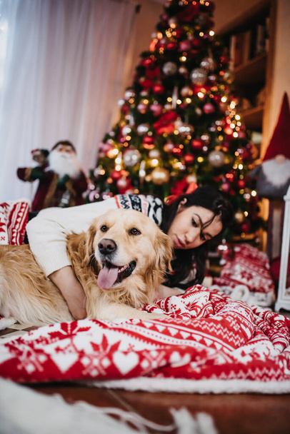 A female playing with her golden retriever dog beside a colorful Christmas Tree at Christmas eve - Foto, afbeelding