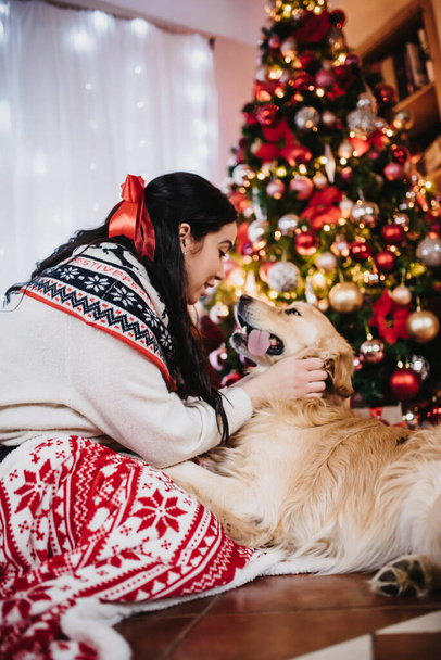 A female playing with her golden retriever dog beside a colorful Christmas Tree at Christmas eve - Fotó, kép