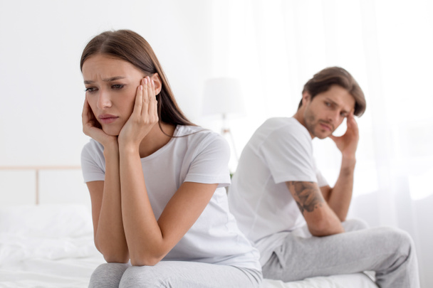 Molesto ofendido millennial europeo esposa sentado en la cama ignorando triste marido en blanco dormitorio - Foto, imagen