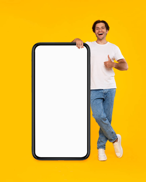 Happy man showing white empty smartphone screen and thumb up - Fotó, kép