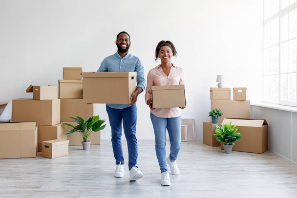 Усміхаючись, африканський чоловік і дружина несуть коробки з речами в новій квартирі, люблять переїжджати. - Фото, зображення