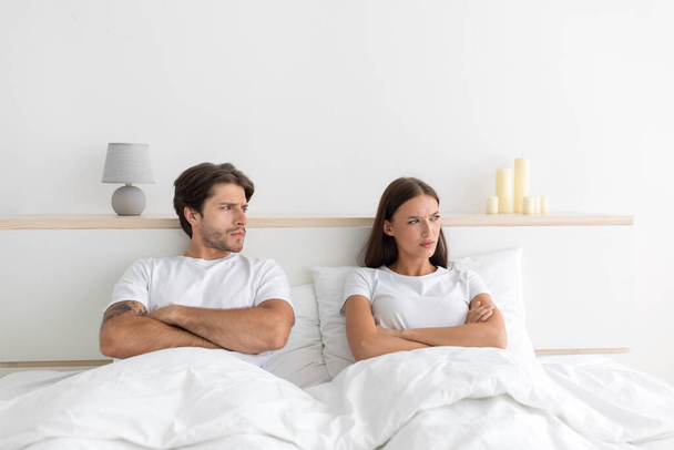 Sad unhappy young european guy with crossed arms on his chest look at offended wife at bed - Photo, Image