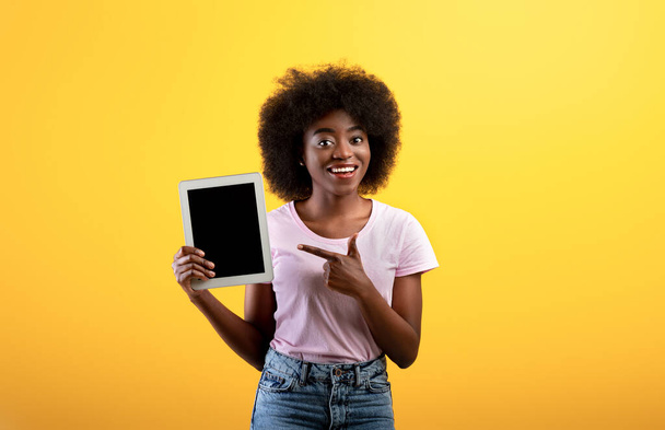 Happy Afro-Amerikaanse dame wijzen naar digitale tablet met blanco scherm, gele achtergrond, mockup - Foto, afbeelding