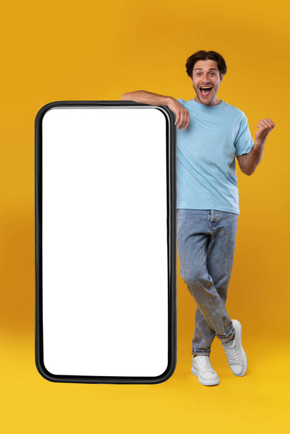 Excited guy leaning on empty smartphone screen and gesturing yes - Photo, Image