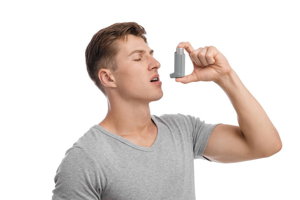 Kalm geconcentreerde duizendjarige blanke aantrekkelijke man die lijdt aan astma en spuiten inhalator in de mond - Foto, afbeelding