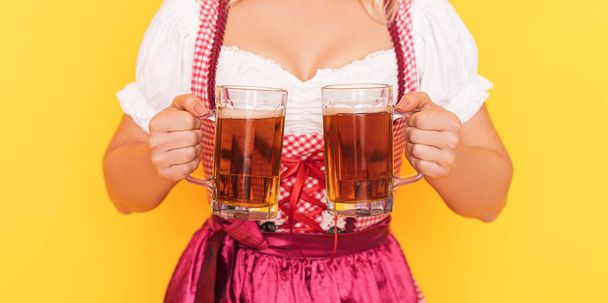 Woman in festive german dress holding two mugs of beer. - Фото, зображення