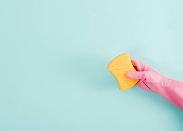 Las manos en guantes de goma rosa sostienen una esponja de lavado. Fondo azul. Concepto de limpieza y limpieza. Puesta plana - Foto, Imagen