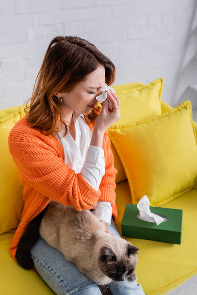 mladá žena trpící alergií při sezení na pohovce s kočkou - Fotografie, Obrázek