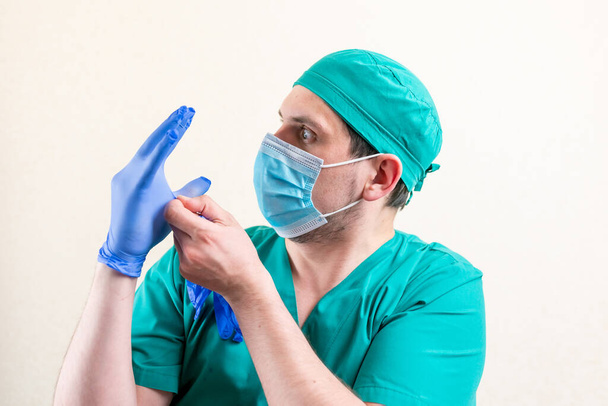 Un médico con una máscara y una gorra, juega con guantes. Foto de alta calidad - Foto, imagen