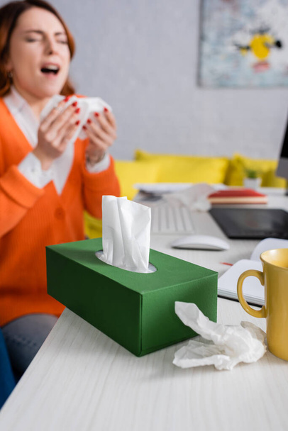 selective focus of pack with paper napkins near sick woman sneezing on blurred background - Valokuva, kuva