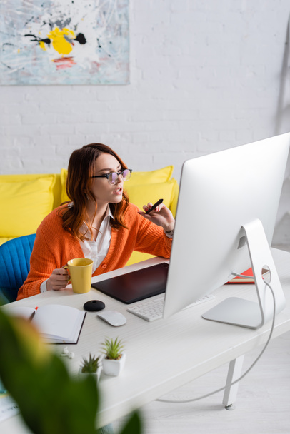 retoucher s šálkem čaje ukazuje na monitor s stylus při práci doma - Fotografie, Obrázek