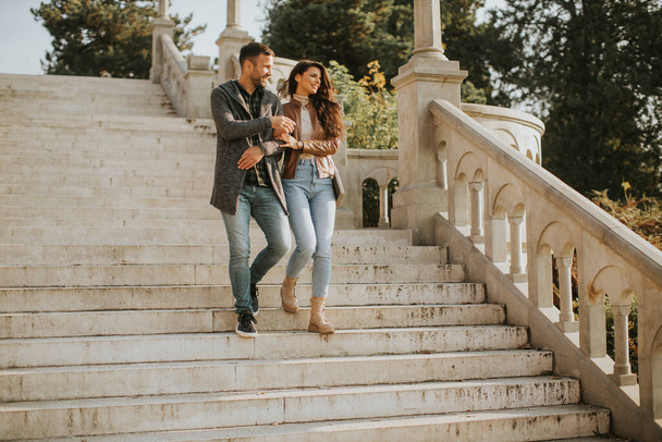 Hübsches junges Paar lächelt und spricht, während es an einem Herbsttag die Außentreppe hinunterschlendert - Foto, Bild