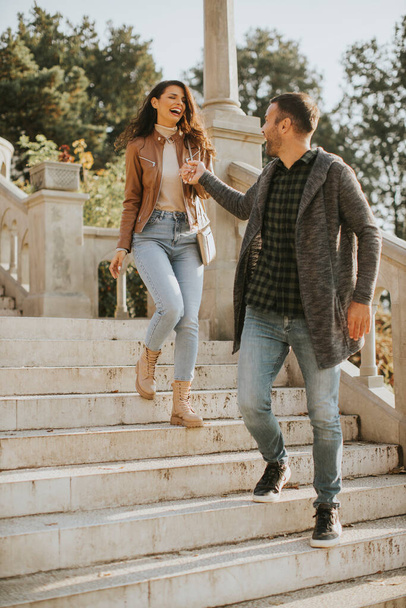 Pretty young couple smiling and talking while strolling down outdoor stairs on autumn day - Photo, image