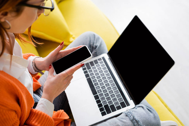 bijgesneden weergave van wazig vrouw houden laptop met leeg scherm terwijl zitten op de bank met laptop - Foto, afbeelding
