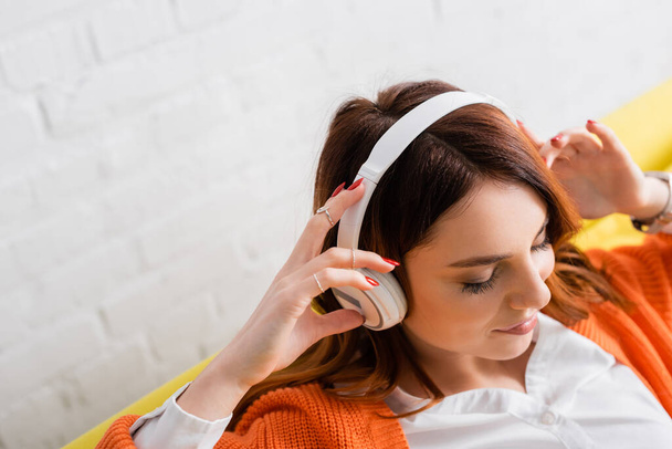 high angle view of pleased young woman with closed eyes listening music in headphones - 写真・画像