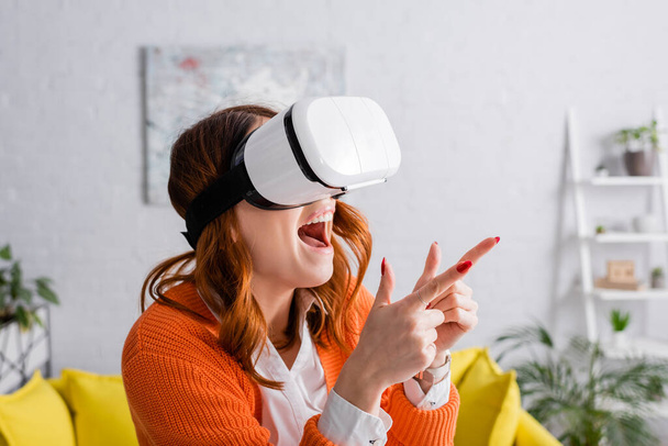 excited woman in vr headset pointing with fingers while gaming at home - Photo, image