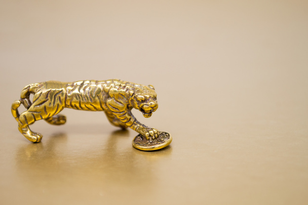 A bronze figure of a tiger with a coin - the symbol of the Chinese new year 2022 on a golden background, copy space. Wishes of good luck, financial well-being and wealth. - Photo, Image