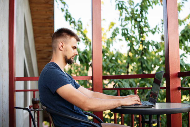 Um jovem barbudo está usando laptop de computador para trabalhar ao ar livre, trabalhando projeto freelancer on-line ao ar livre em casa, estudante bonito estudar, aprender, educação on-line, freelancer - Foto, Imagem