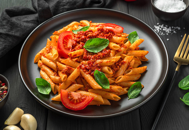 Traditional Italian penne pasta with bolognese sauce and fresh basil on a black background. Side view, close-up. - Valokuva, kuva