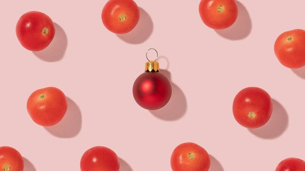 Δημιουργική σύνθεση μοτίβο με φρέσκα ντοματίνια και κόκκινο στολίδι Χριστουγέννων σε φωτεινό ροζ φόντο. - Φωτογραφία, εικόνα