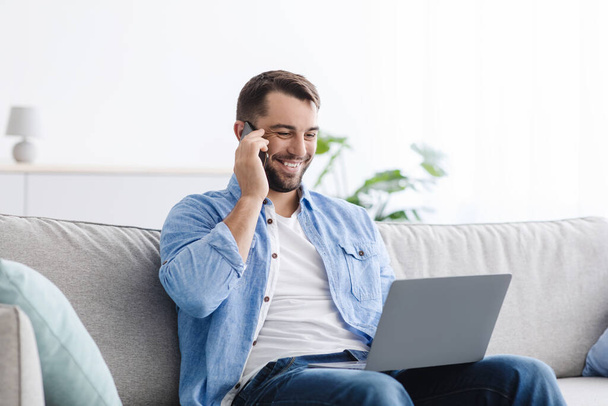 Veselý pohledný dospělý Evropan chlap mají hovor s klientem, pracuje na notebooku v obývacím pokoji interiéru - Fotografie, Obrázek