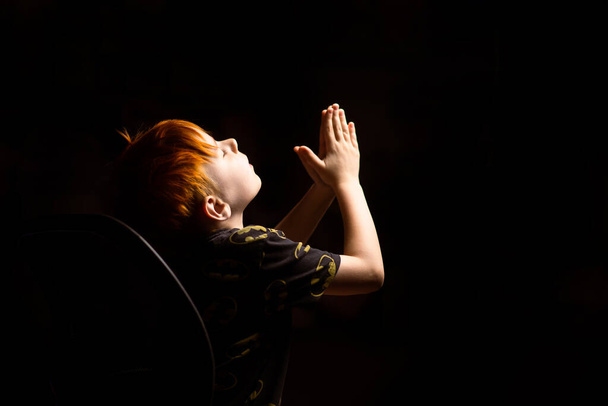 Nuori punatukkainen poika rukoilee pimeässä. - Valokuva, kuva