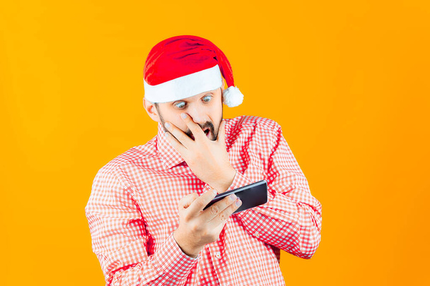 a man wearing a Santa Claus hat looks shocked into the phone - Photo, Image