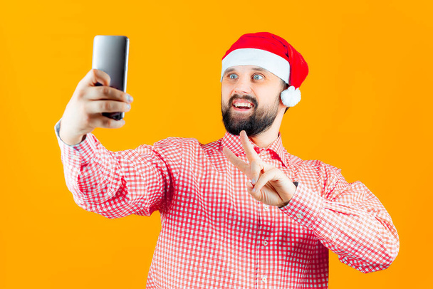 cheerful man in a santa claus hat makes christmas selfies - Foto, afbeelding