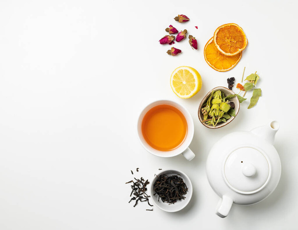 Flat colocar uma xícara de chá preto, frutas e chá de ervas, com limão e panela de chá em um fundo branco. O conceito de uma bebida saudável. Vista superior e espaço de cópia. - Foto, Imagem