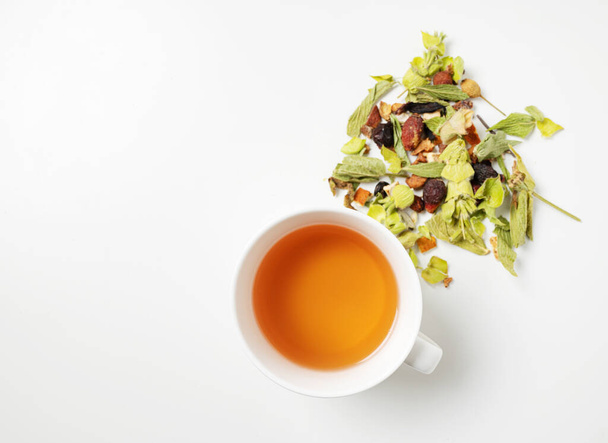 A cup of herbal tea with scattered dried herbs and pieces of fruit on a white background. Top view and copy space. - Foto, immagini