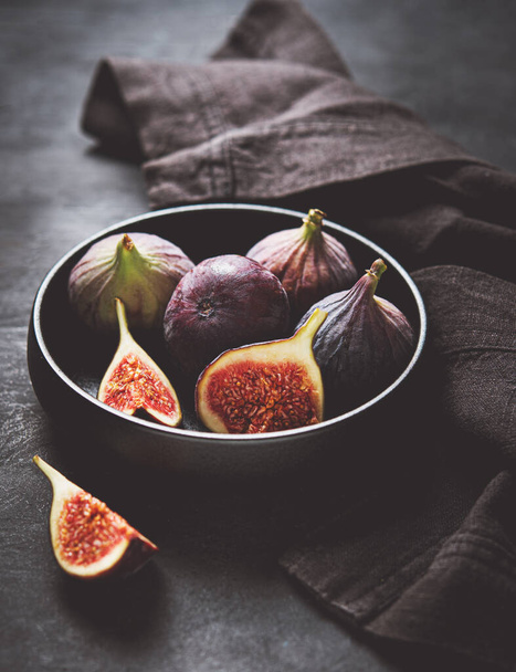 Fresh ripe figs in a black bowl on a dark gray background close-up. Dark and mood concept. Tint image. - Photo, Image